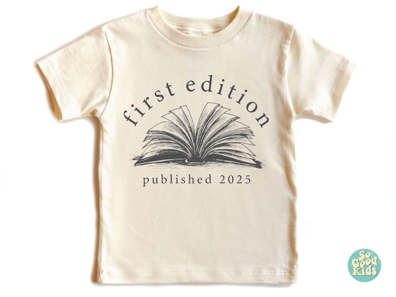 May include: A cream-colored short-sleeved t-shirt with a black and white illustration of an open book. The text "first edition published 2025" is printed on the shirt.