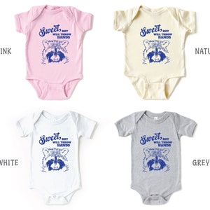 Op de afbeelding: Vier baby rompertjes in verschillende kleuren: roze, naturel, wit en grijs. Elk rompertje heeft een blauwe afbeelding van een wasbeer met de tekst "Sweet, but will throw hands".