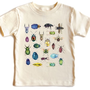 May include: A beige organic cotton t-shirt for kids featuring a colorful illustration of various types of beetles. The shirt has short sleeves and a crew neck. The text "So Good Kids" is printed on the bottom right corner of the shirt.