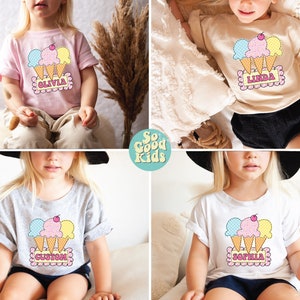 May include: Four children's t-shirts with a colorful ice cream cone graphic and a personalized name. The shirts are in pink, beige, grey, and white.