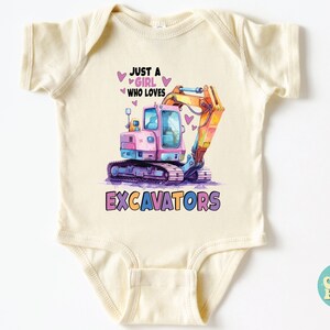 May include: Cream-colored baby bodysuit with a colorful excavator graphic. The design features a pink and blue excavator with the text "JUST A GIRL WHO LOVES EXCAVATORS". Hearts are scattered around the text and excavator.