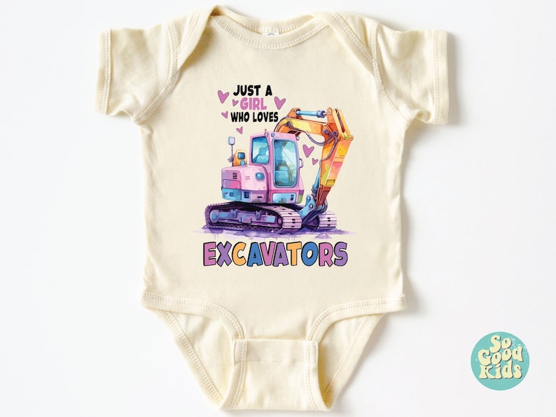 May include: Cream-colored baby bodysuit with a colorful excavator graphic. The design features a pink and blue excavator with the text "JUST A GIRL WHO LOVES EXCAVATORS". Hearts are scattered around the text and excavator.