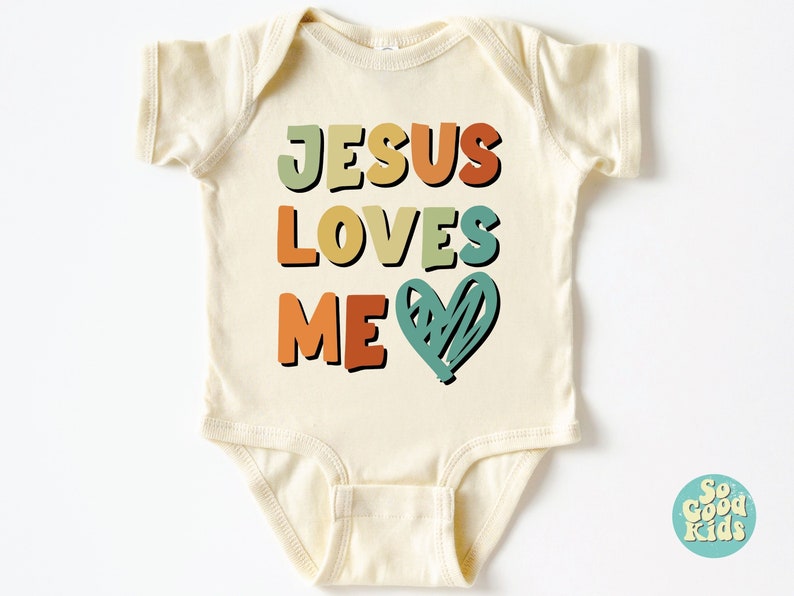 Puede incluir: Un body de beb&eacute; de color crema con el texto "JESUS LOVES ME" en letras retro de colores y un coraz&oacute;n verde.