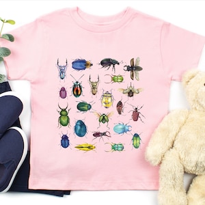 May include: A pink t-shirt featuring a colourful illustration of various beetles. The beetles are depicted in a range of colours, including green, blue, red, yellow, and black.