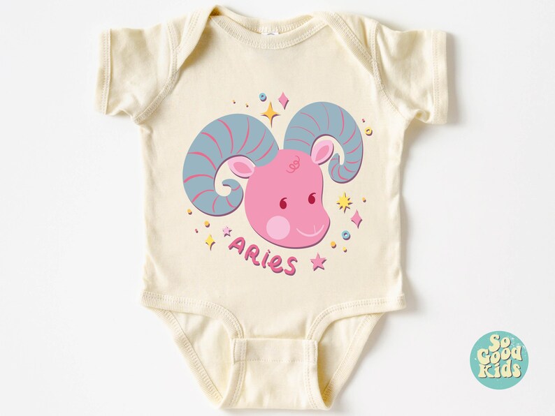 May include: A cream-coloured baby onesie with a pink and blue cartoon ram with the word "Aries" written below it.