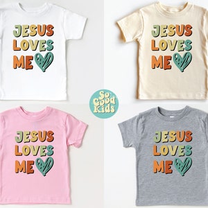 Puede incluir: Cuatro camisetas para ni&ntilde;os peque&ntilde;os con el texto "JESUS LOVES ME" en letras retro de colores y un coraz&oacute;n verde. Las camisetas son blancas, beige, rosas y grises.