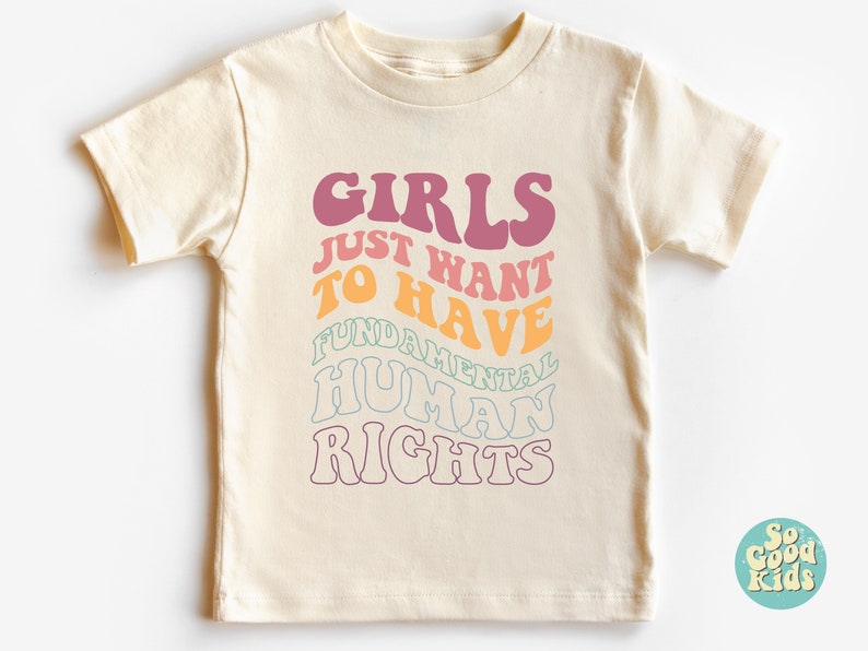 May include: A light beige t-shirt with a colorful graphic that reads "Girls Just Want To Have Fundamental Human Rights".