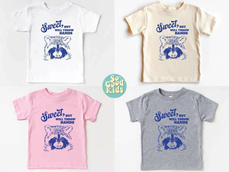 Op de afbeelding: Vier t-shirts in peutermaat met een wasbeer-afbeelding en de tekst "Sweet, but will throw hands". De shirts zijn in wit, beige, roze en grijs.