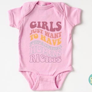 May include: Pink baby onesie with the text "Girls Just Want To Have Fundamental Human Rights" in a rainbow color scheme.