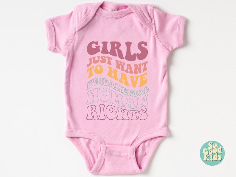 May include: Pink baby onesie with the text "Girls Just Want To Have Fundamental Human Rights" in a rainbow color scheme.