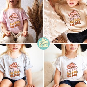 K&ouml;nnte beinhalten: Vier T-Shirts f&uuml;r Kinder mit einem rosafarbenen Cowgirl-Hut und dem dreimal wiederholten Text "Yee Haw". Die Shirts sind in rosa, beige, grau und wei&szlig;.
