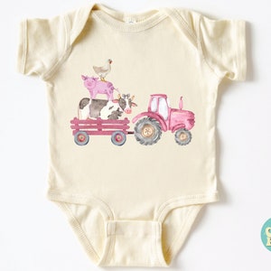 May include: Cream-colored baby onesie featuring a watercolor illustration of a pink tractor pulling a wagon with a cow, pig, and chicken. The design has a farm theme, perfect for a baby.