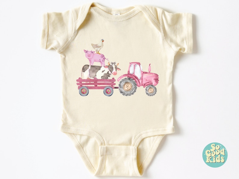 May include: Cream-colored baby onesie featuring a watercolor illustration of a pink tractor pulling a wagon with a cow, pig, and chicken. The design has a farm theme, perfect for a baby.