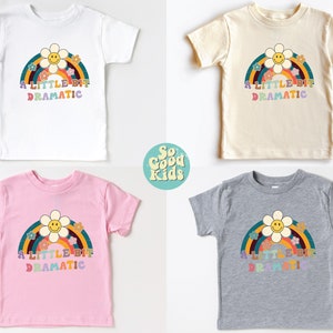 Pode incluir: Quatro camisetas para crian&ccedil;as pequenas em diferentes cores com um arco-&iacute;ris e uma margarida com um rosto sorridente. O texto nas camisetas diz "A Little Bit Dramatic".