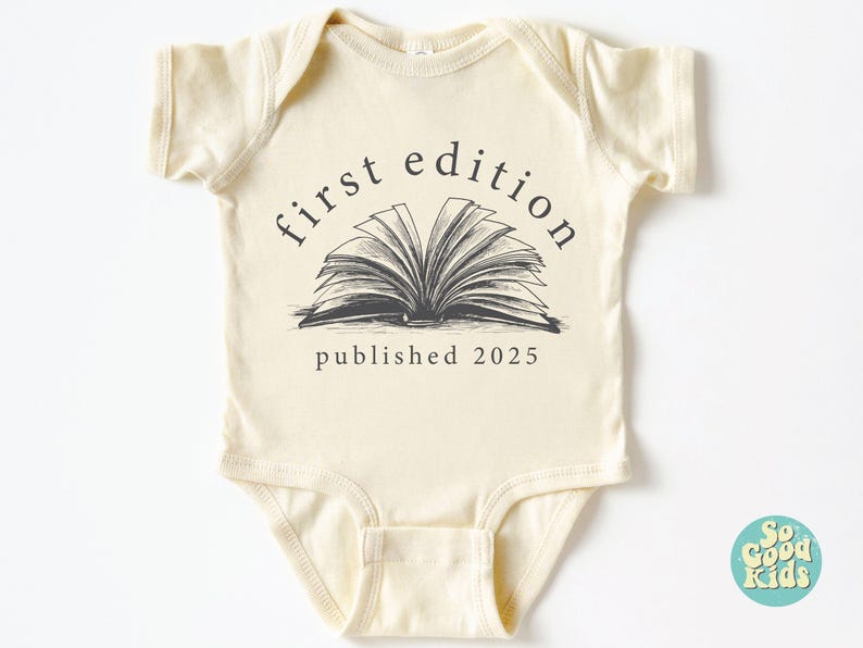 May include: A cream-colored baby onesie with short sleeves features a black and white illustration of an open book with the text "first edition published 2025".