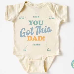 May include: A cream-colored baby onesie with the text "YOU GOT THIS DAD!" in blue and orange lettering. The onesie has a diagram showing the front, head, arms, and legs.