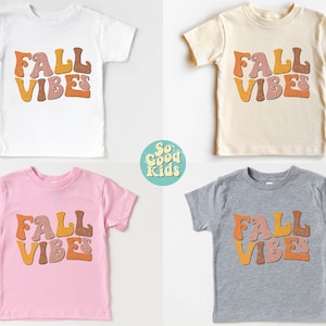 Puede incluir: Cuatro camisetas para ni&ntilde;os peque&ntilde;os en diferentes colores con el texto "Fall Vibes" en una fuente retro. Las camisetas son blancas, beige, rosas y grises.