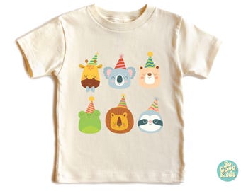 May include: A cream colored t-shirt with a graphic of six animals wearing party hats. The animals are a giraffe, koala, bear, frog, lion, and sloth. The text "So Good Kids" is in the lower right corner of the shirt.