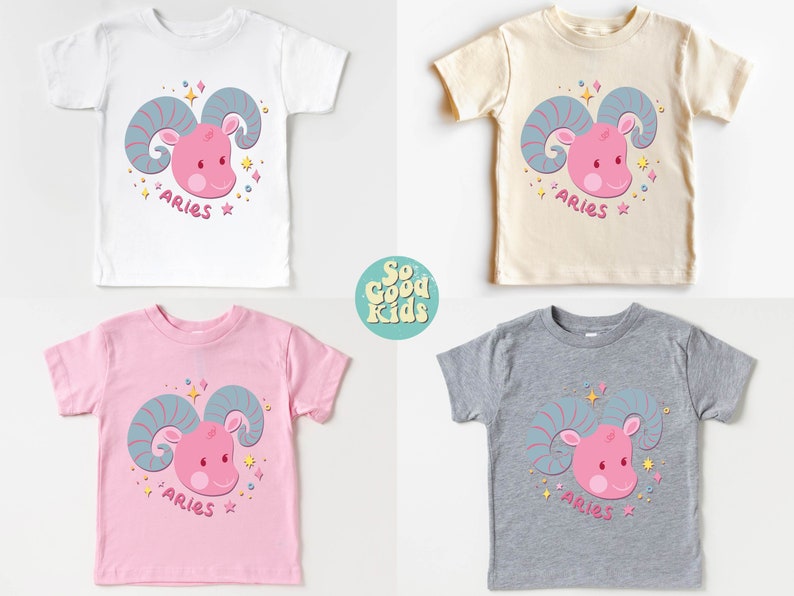 May include: Four toddler-sized t-shirts in white, beige, pink, and grey with a pink cartoon ram head with blue horns and the word "Aries" printed on each shirt.