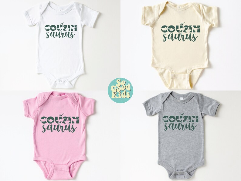 May include: Four baby onesies in different colors: white, cream, pink, and gray. Each onesie has the text "COUSINsaur" printed in dark green with a dinosaur silhouette graphic.