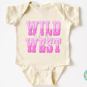 May include: A cream-colored baby onesie with pink lettering that reads "WILD like the WEST". The letters are outlined in white and have a pink floral pattern.