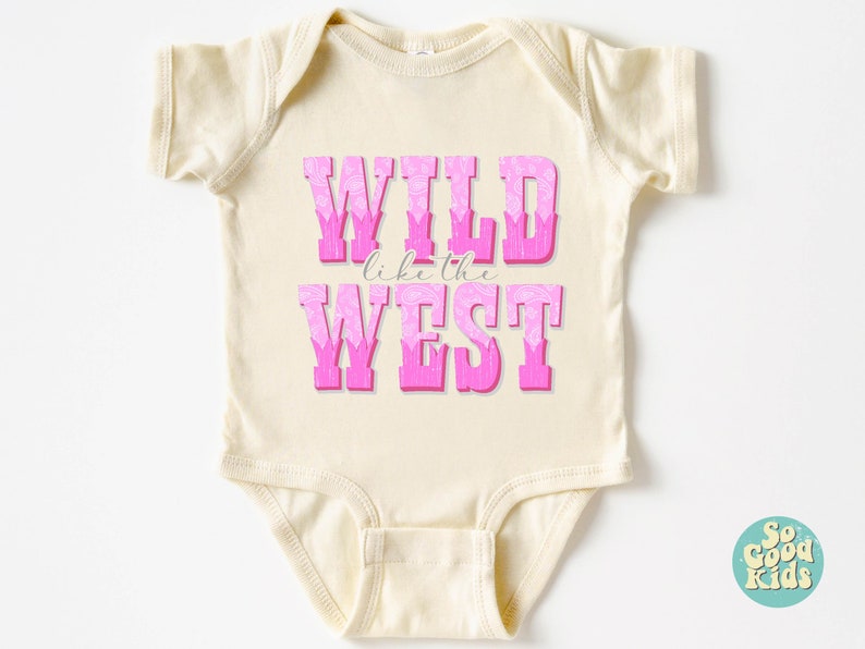 May include: A cream-colored baby onesie with pink lettering that reads "WILD like the WEST". The letters are outlined in white and have a pink floral pattern.