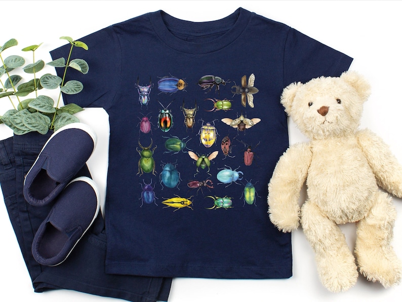 May include: A navy blue t-shirt featuring a colourful pattern of various beetles and insects. The shirt is made from a soft, comfortable material and is ideal for children who love bugs.