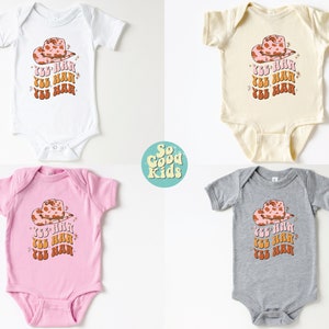 K&ouml;nnte beinhalten: Vier Baby-Bodys in verschiedenen Farben: Wei&szlig;, Beige, Rosa und Grau. Jeder Body zeigt ein Cartoon-Bild eines rosa und braunen Cowboyhuts mit dem Text "Yee Haw", der dreimal in einer Retro-Schrift wiederholt wird.