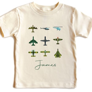 May include: A cream colored t-shirt with a green print of different types of airplanes. The text "James" is printed in green below the airplanes.