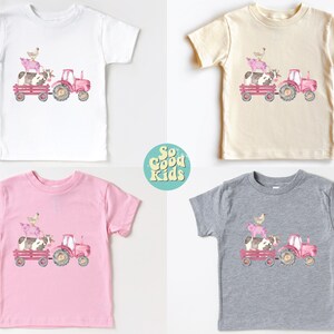 May include: Four children's t-shirts in white, beige, pink, and gray, each featuring a watercolor illustration. The design shows a pink tractor pulling a wagon with a cow, pig, and chicken. The text "So Good Kids" is in a circle.