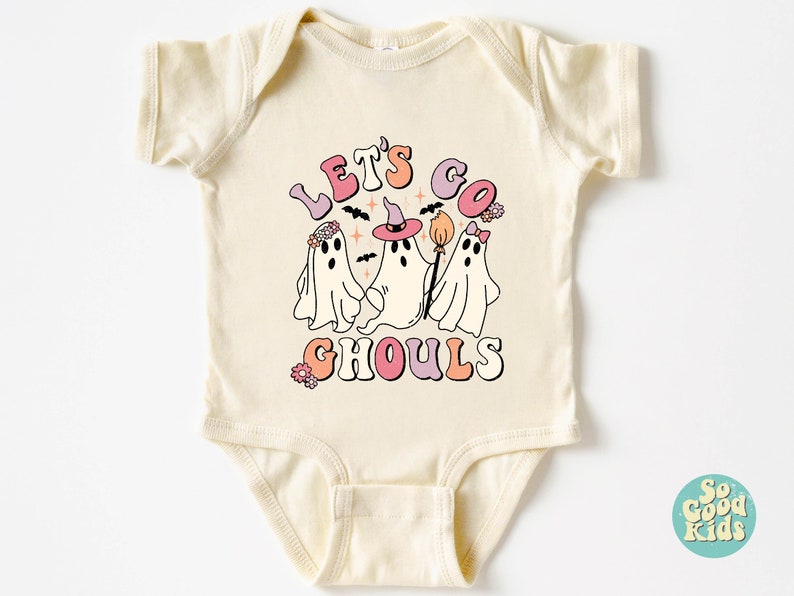 May include: A cream-colored baby onesie with a graphic of three ghosts wearing witch hats and flowers. The text "Let's Go Ghouls" is written in pink, orange, and blue letters.