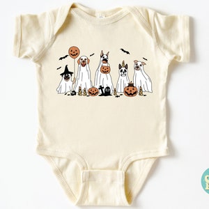 Puede incluir: Un body de beb&eacute; de color crema con un gr&aacute;fico de cinco perros disfrazados de fantasmas para Halloween. Los perros sostienen calabazas y un globo. El texto "So Good Kids" es visible en la esquina inferior derecha de la imagen.