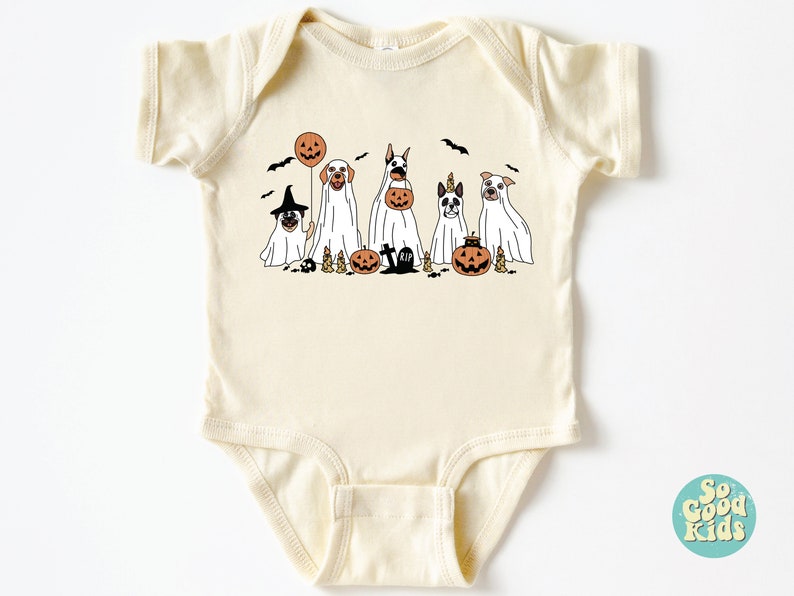 Puede incluir: Un body de beb&eacute; de color crema con un gr&aacute;fico de cinco perros disfrazados de fantasmas para Halloween. Los perros sostienen calabazas y un globo. El texto "So Good Kids" es visible en la esquina inferior derecha de la imagen.