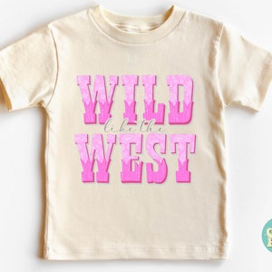 May include: A cream colored t-shirt with a pink graphic that says "WILD like the WEST".