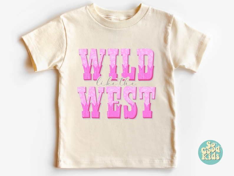 May include: A cream colored t-shirt with a pink graphic that says "WILD like the WEST".