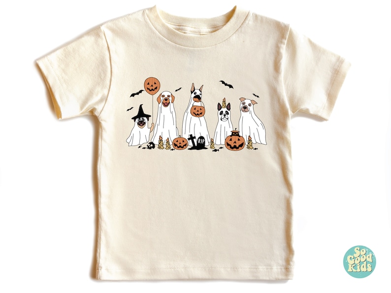 Puede incluir: Una camiseta blanca con un gr&aacute;fico de cinco perros disfrazados de fantasmas para Halloween. Los perros sostienen calabazas y cubos de dulces. El texto "So Good Kids" est&aacute; en la esquina inferior derecha de la imagen.