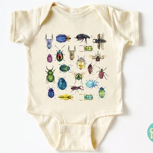 May include: A cream-coloured baby onesie with a colourful pattern of various beetles. The onesie has short sleeves and a snap closure. The text "So Good Kids" is printed on a blue circle in the bottom right corner.
