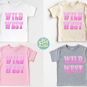 May include: Four t-shirts with the text "WILD like the WEST" in pink letters on a white, beige, pink, and gray background. The shirts are all short-sleeved and have a crew neck.