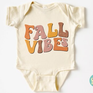 May include: A cream-colored baby onesie with the text "FALL VIBES" in a retro font with orange, brown, and pink colors.
