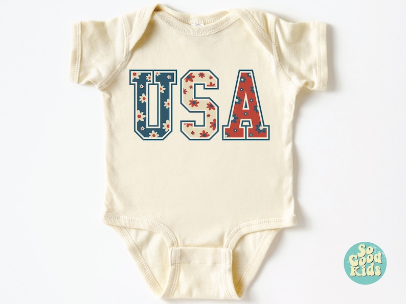 K&ouml;nnte beinhalten: Ein cremefarbener Baby-Strampler mit kurzen &Auml;rmeln zeigt eine Grafik im Vintage-Stil des Wortes "USA" in Blau und Rot mit einem floralen Muster.