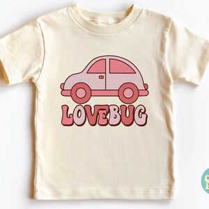 May include: A cream colored t-shirt with a pink cartoon car and the text "LOVEBUG" in pink and red letters.