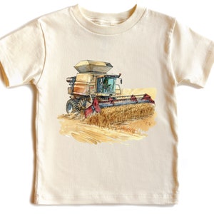 May include: A beige short-sleeved t-shirt with a watercolor illustration of a combine harvester in a field of wheat.