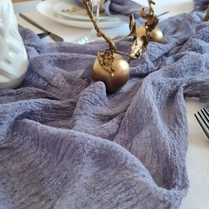 Può includere: Un runner da tavolo in lino grigio con due ornamenti decorativi dorati. Gli ornamenti hanno la forma di mele con un ramoscello e foglie.