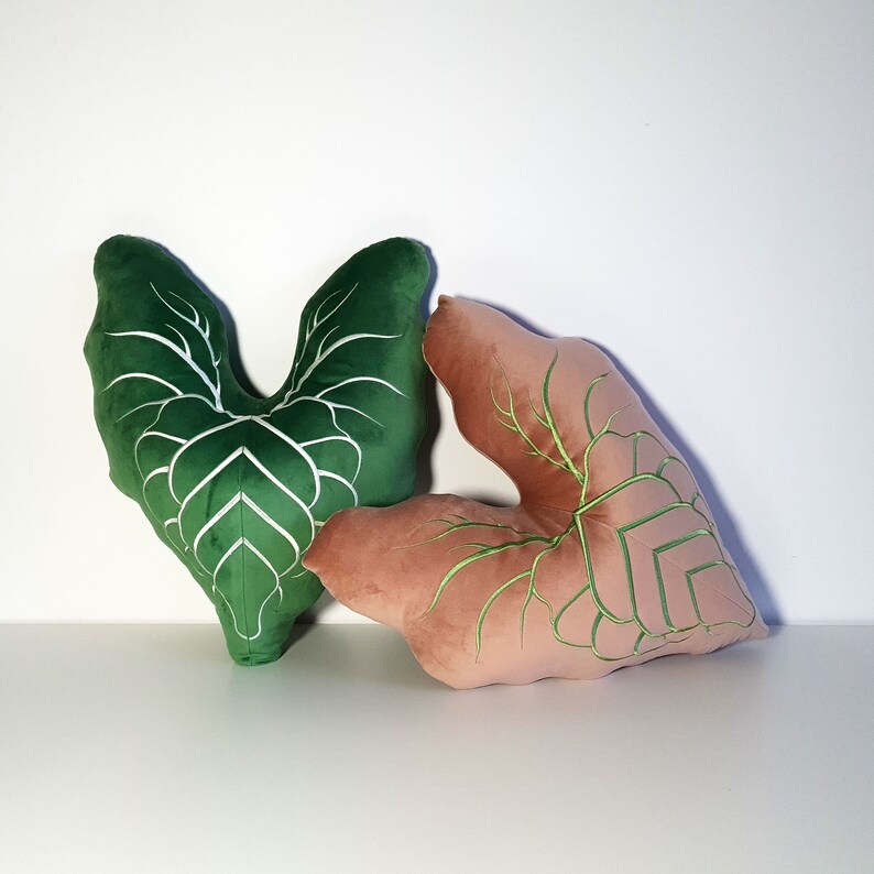 May include: Two decorative pillows shaped like leaves. One pillow is green with white veins and the other is pink with green veins.