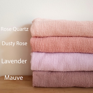 Puede incluir: Una pila de cuatro telas suaves y texturizadas en tonos rosa y morado. Las telas están etiquetadas como "Rose Quartz", "Dusty Rose", "Lavender" y "Mauve". Las telas están apiladas sobre una superficie de madera contra un fondo blanco.