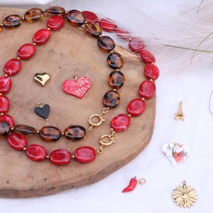 May include: A necklace with red and tortoise-shell beads, gold clasps, and various charms. Charms include a gold heart, a red heart with the word "Love", a black heart, a red chili pepper, a gold Eiffel Tower, a white heart with the word "Love", and a gold sunflower.