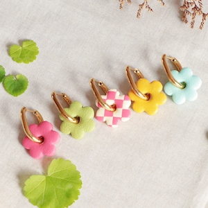 Puede incluir: Cinco pares de pendientes de aro dorados con abalorios de flores de colores. Los abalorios son de color rosa, verde, amarillo, blanco y azul.