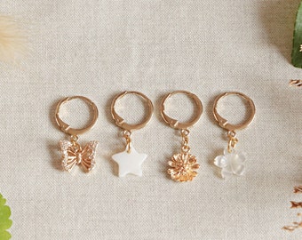 May include: Four gold hoop earrings with different charms: a butterfly, a star, a flower, and a flower. The charms are made of white shell.