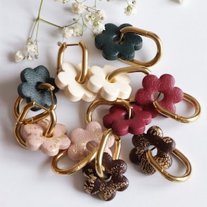 May include: A set of eight gold hoop earrings with flower-shaped charms. The charms are in various colours, including green, white, red, pink, and brown. Each charm has a different pattern.