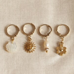 May include: Four gold hoop earrings with different charms: a white seashell, a gold sun with a face, a white pearl, and a gold flower.
